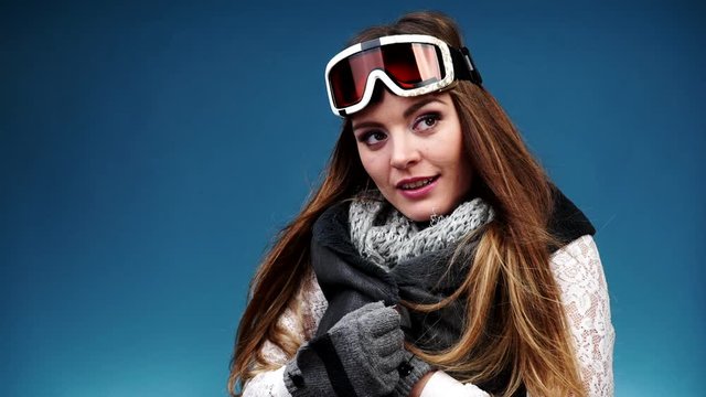 Woman smiling skier girl wearing warm clothing ski goggles portrait. Winter sport activity. Beautiful long hair sportswoman on blue studio shot, full HD.