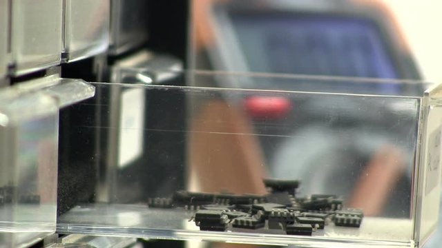 Close-up of hand opening electronic component draw bin to get surface mount micro-controllers.  Components grabbed with tweezers, draw closes.  DVM voltage/current meter is visible in background.