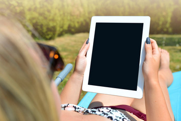 Woman lying on lounger in garden and using digital teblet.