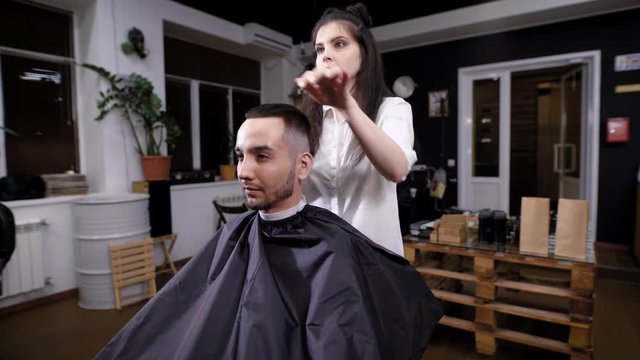 A woman hairdresser completes hair styling for a visitor of a barbershop, a hair stylist uses a gel for styling to shape the hairstyle