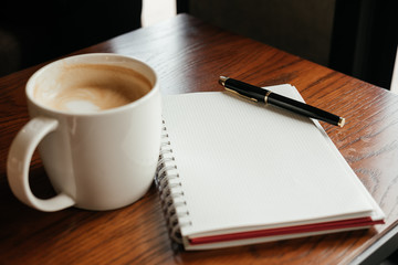 top view. coffee cup with coffee. pen putting on blank notebook. have wooden table are background. image for beverage,business,education concept