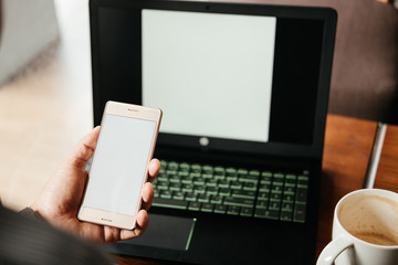 business man holding smartphone and blank screen. laptop notebook and coffee cup put on wooden table at workplace. image for technology,mobile,computer,business,education concept