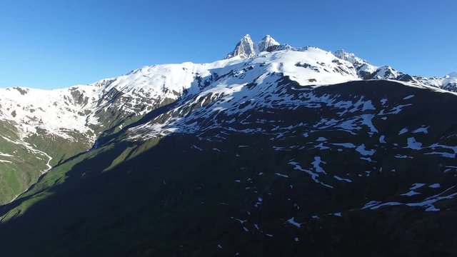Aerial view of the mountain plateau next to peak of Ushba, among the snow-capped mountain ranges in the rays of the rising sun, Svaneti, Georgia.