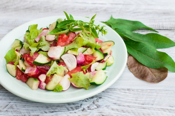 Salad of fresh vegetables, sliced tomatoes, cucumbers and lettuce leaves on a plate. Close-up.