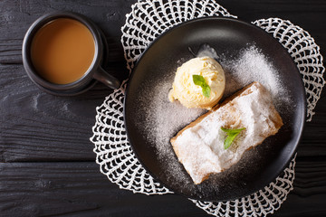 Apple strudel with vanilla ice cream on a plate and coffee with milk close-up. Horizontal top view