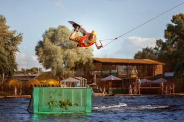 Male skateboarder jumps over a springboard on a lake, he is an extreme sportsman.
