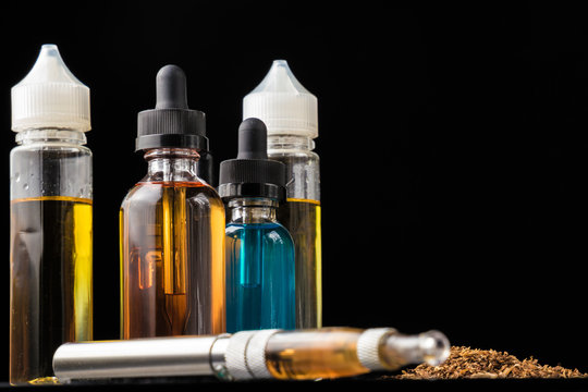 E-liquid bottles and e-cigarette with pile of grinded tobacco leaves