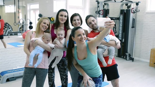 Young parents and babies in modern gym taking selfie.