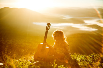 Young girl meets sunrise on top of a mountain with a guitar