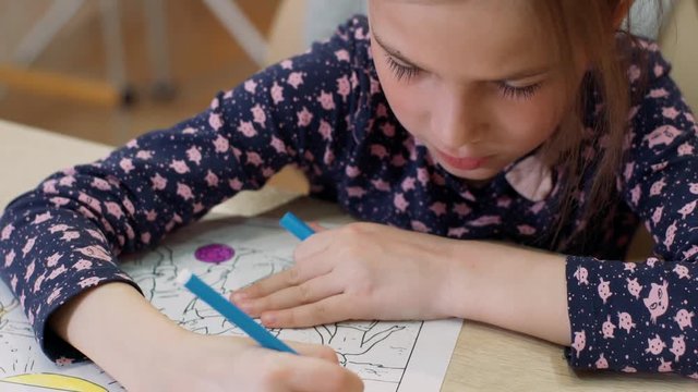 The girl paints the coloring with a felt-tip pen