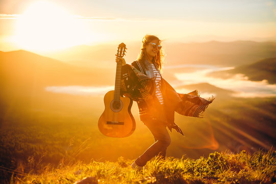 Young girl meets sunrise on top of a mountain with a guitar 