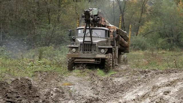 Dirty truck with a mounted crane is hauling logs through mud in the forest