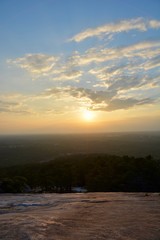 View of a sunset from the top of a mountain with soft light reflecting on the rock on the mountain with blue orange sky and white clouds