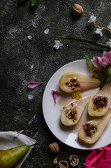 baked pears with cranberry, cheese on white plates with assorted flowers and nuts on a green background, top view