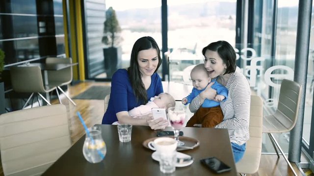 Women with babies in cafe, looking at pictures in smart phone.