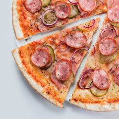 Sliced pizza with sausages, onions and pickles