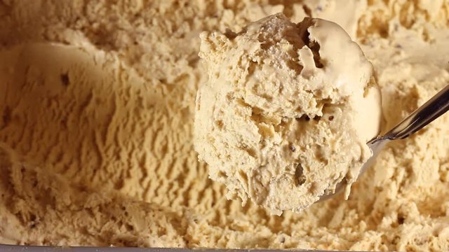 Taking a scoop of ice cream from the box. Close-up of caramel ice cream in a large box. Round spoon makes shoelaces balls for buyers