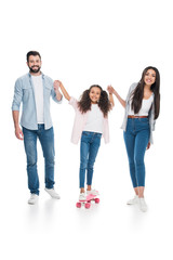 Obraz premium Happy parents holding hands of cute little daughter standing on skateboard