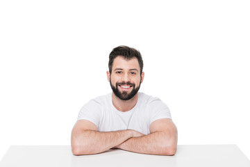 Handsome young bearded man sitting at table and smiling at camera