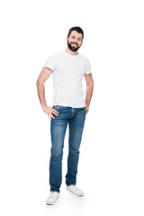 Bearded young man in white t-shirt standing with hands on hips and smiling at camera