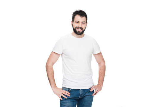 Bearded Young Man In White T-shirt Standing With Hands On Hips And Smiling At Camera