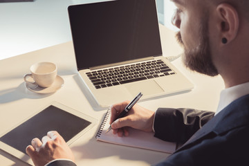 Cropped shot of businessman using digital tablet and taking notes while sitting at workplace