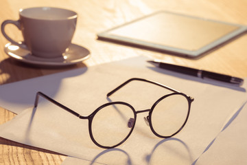 Close-up view of digital tablet with eyeglasses, cup of coffee and papers on table