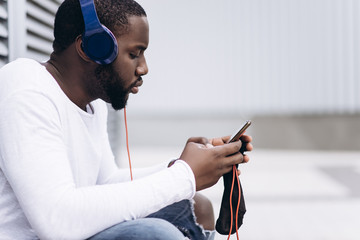 Handsome Afro American man wearing casual clothes in modern city listening to music with headphones