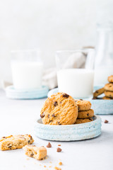 Chocolate chip cookies on blue stone plate with glass of milk on light gray background. Selective focus. Copy space.