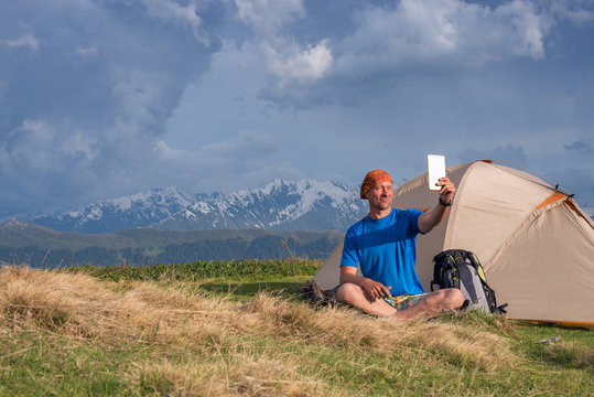 Happy traveler sit next to tent and taking selfie