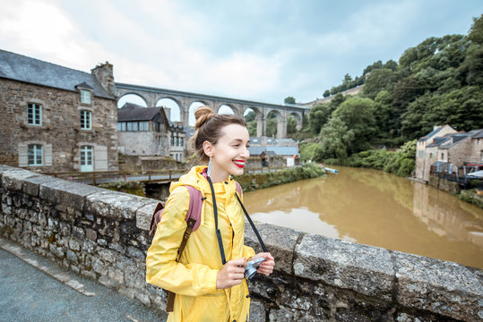 Young woman in yellow raincoat traveling with backpack and photo camera in Dinan village at Brittany region in France