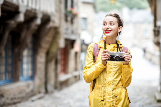Young woman in yellow raincoat walking with backpack and photo camera in Dinan village at Brittany region in France