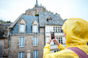 Young woman in yellow raincoat photographing buildings visiting a famous Mont Saint Michel island in France