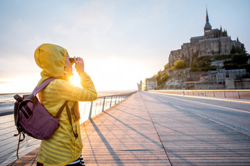 Young female traveler in yellow raincoat on the road to famous saint Michel island in France