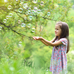Cute little girl on a forest glade among lush vegetation and around fly soap bubbles. Kid wih soap bubbles over nature outdoor.