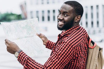 Handsome and happy Afro American tourist with old camera and map in modern city with map in hands and looking at the camera