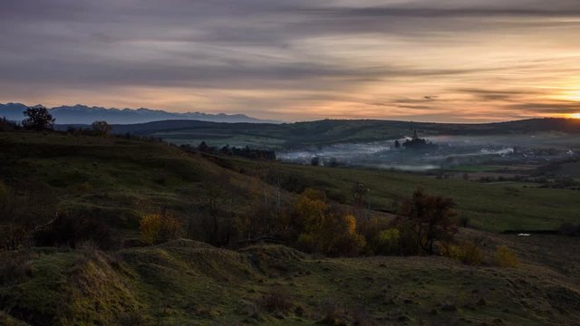 Cincu village with fortified medieval church and a quiet countryside landscape at sunset. Fagaras Mountains in background. 4k time lapse. 