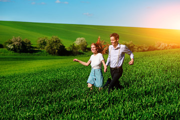 Young happy lovers running on meadow with green grass and blue sky