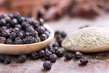 black peppercorns and black pepper powder on wooden spoon.