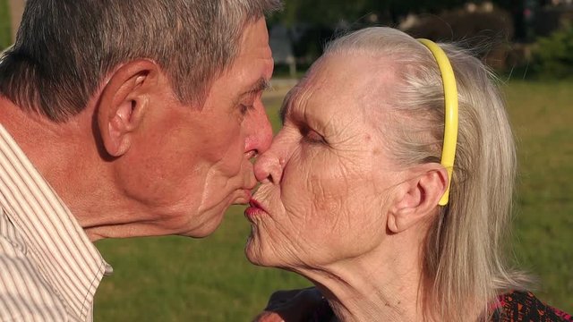 An elderly grandfather of eighty years old kisses his wife in the park close-up. Portrait of kissing grandparents in the park.