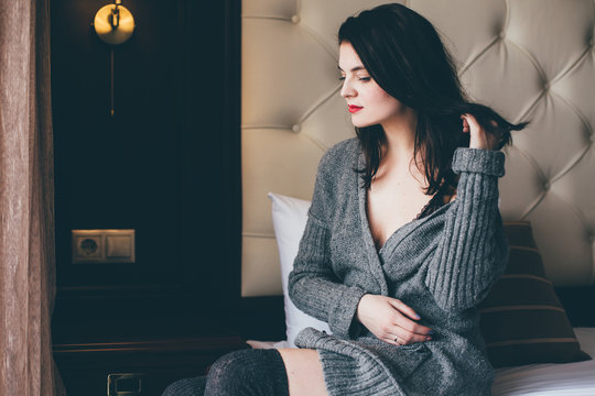 Young Beautiful Woman In A Grey Sweater And Socks Posing In A Cozy Bedroom