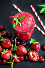 Glass with two straws filled with strawberry smoothie on black with strawberries.