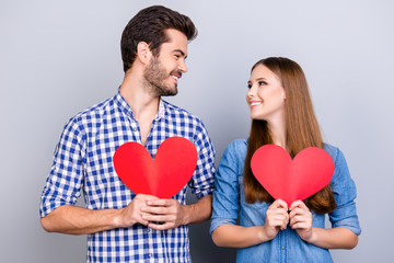 Fototapeta na wymiar Love story. Trust and feelings, emotions and joy. Happy young couple in love is posing, wearing casual shirts, holding big red papers hearts and smiling on the pure background