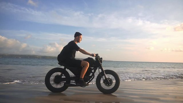 Motorcyclist driving his motorbike on the beach during sunset