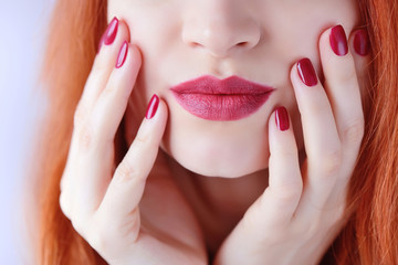 Beautiful red-haired young woman with red manicure, lipstick same color. Close up Portrait.