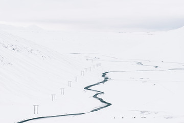 Icelandic winter minimalism: aerial view of a glacial wild river with some farm horses pasturing nearby in the snow