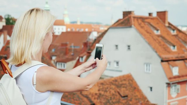 A woman tourist takes pictures of the old part of the beautiful city of Graz. In the picture are visible red tile roofs of the city and old houses. Tourism in Europe