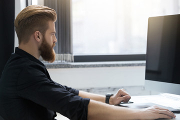 Side view of a young bearded man sitting at his desk