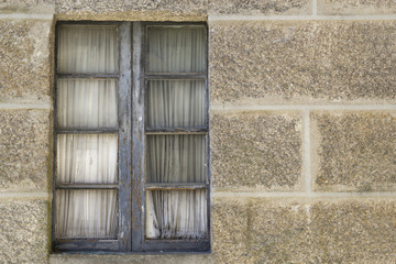 Old window in wooden frame with curtains on a stone wall