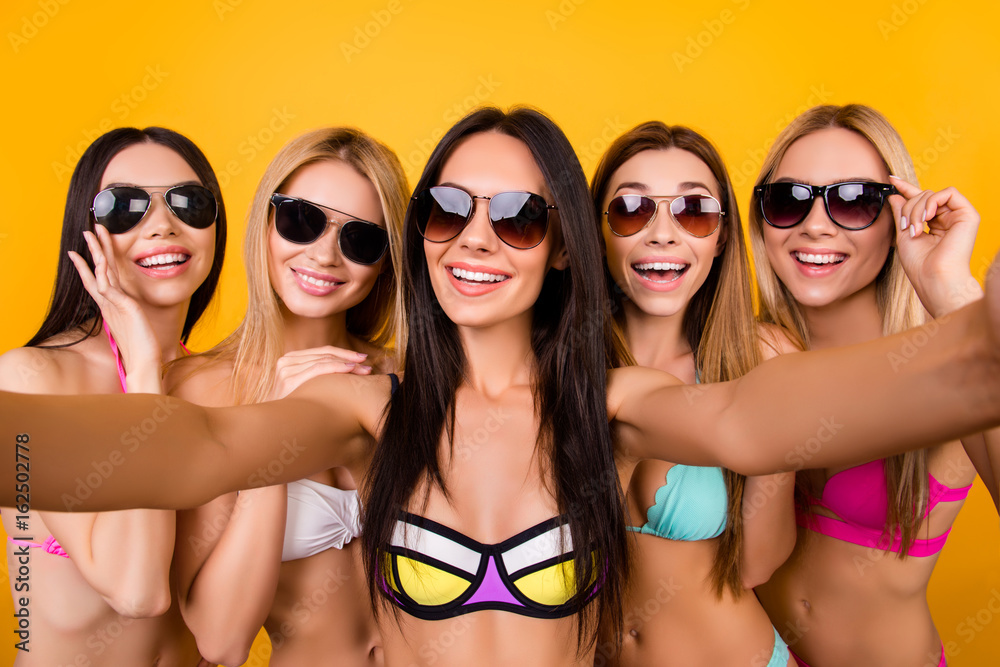 Poster Selfie time, ladies! Five girlfriends in fashionable different swim suits and sunglasses are posing for a selfie photo, that brunette is taking. They are all with beaming smiles,, making memories